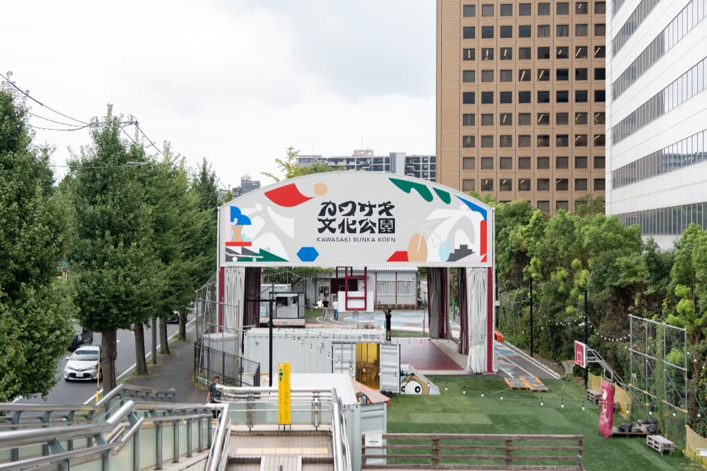 「カワサキ文化公園」と書かれたアーチの門と、その奥に広がる人工芝の広場